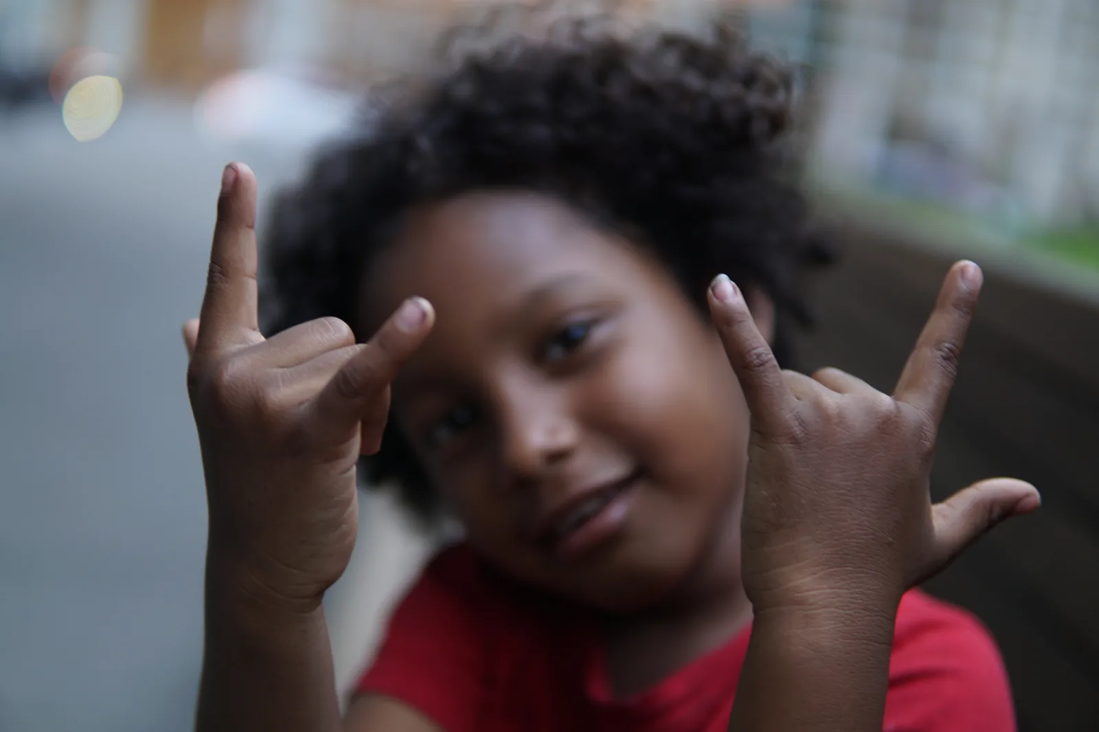 A grinning child holding up both hands in horn gestures on a New York street